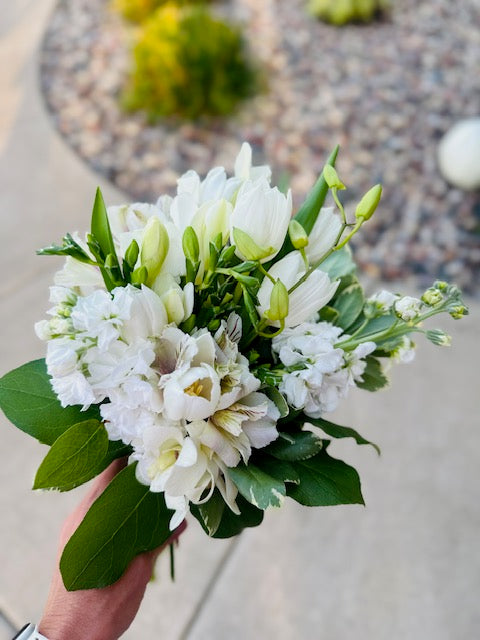 A person holding a DIY posy bouquet with a variety of flowers including gerberas and roses, predominantly in pink and white colors.
