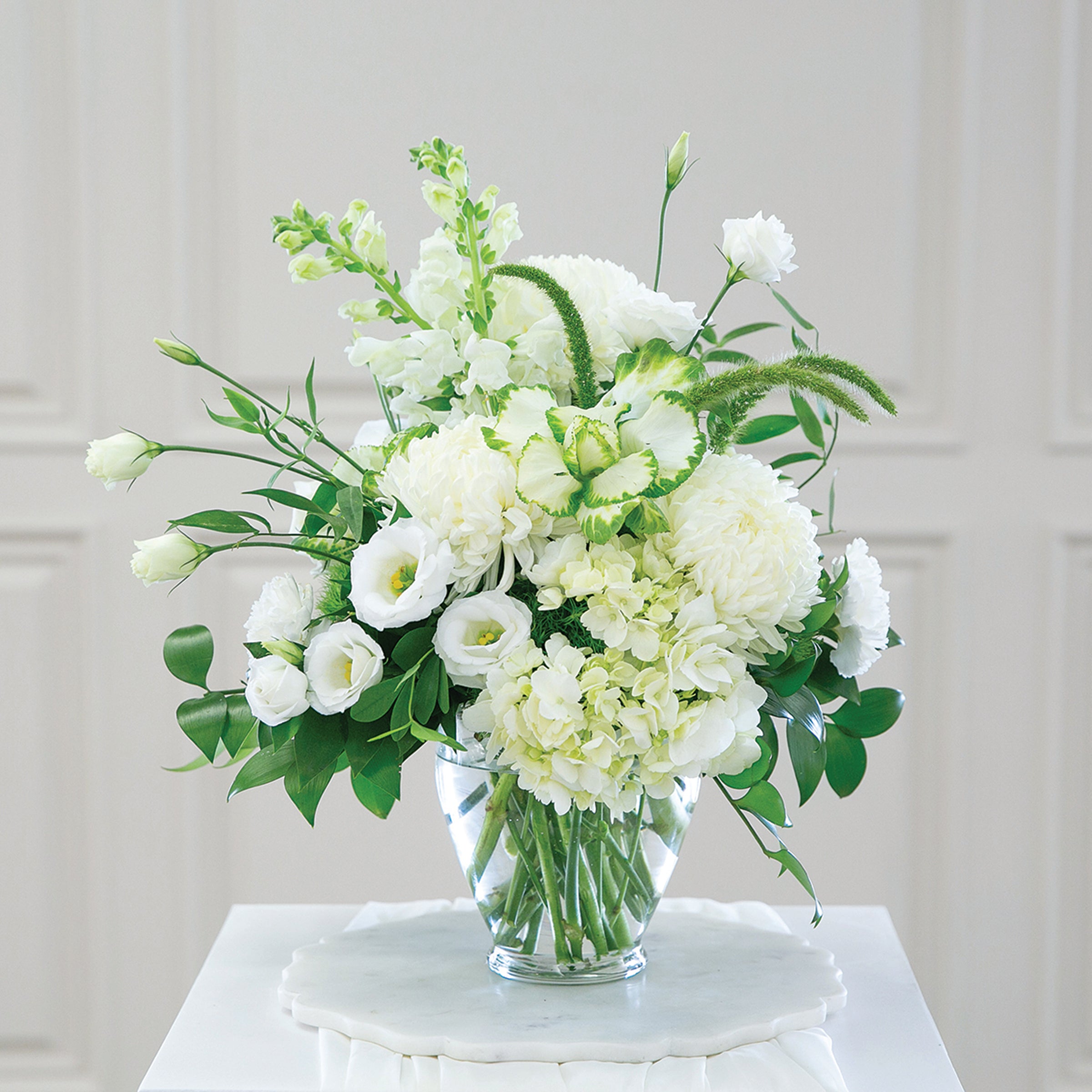 Bouquet of white and green flowers in a clear vase on a white surface with a light gray background