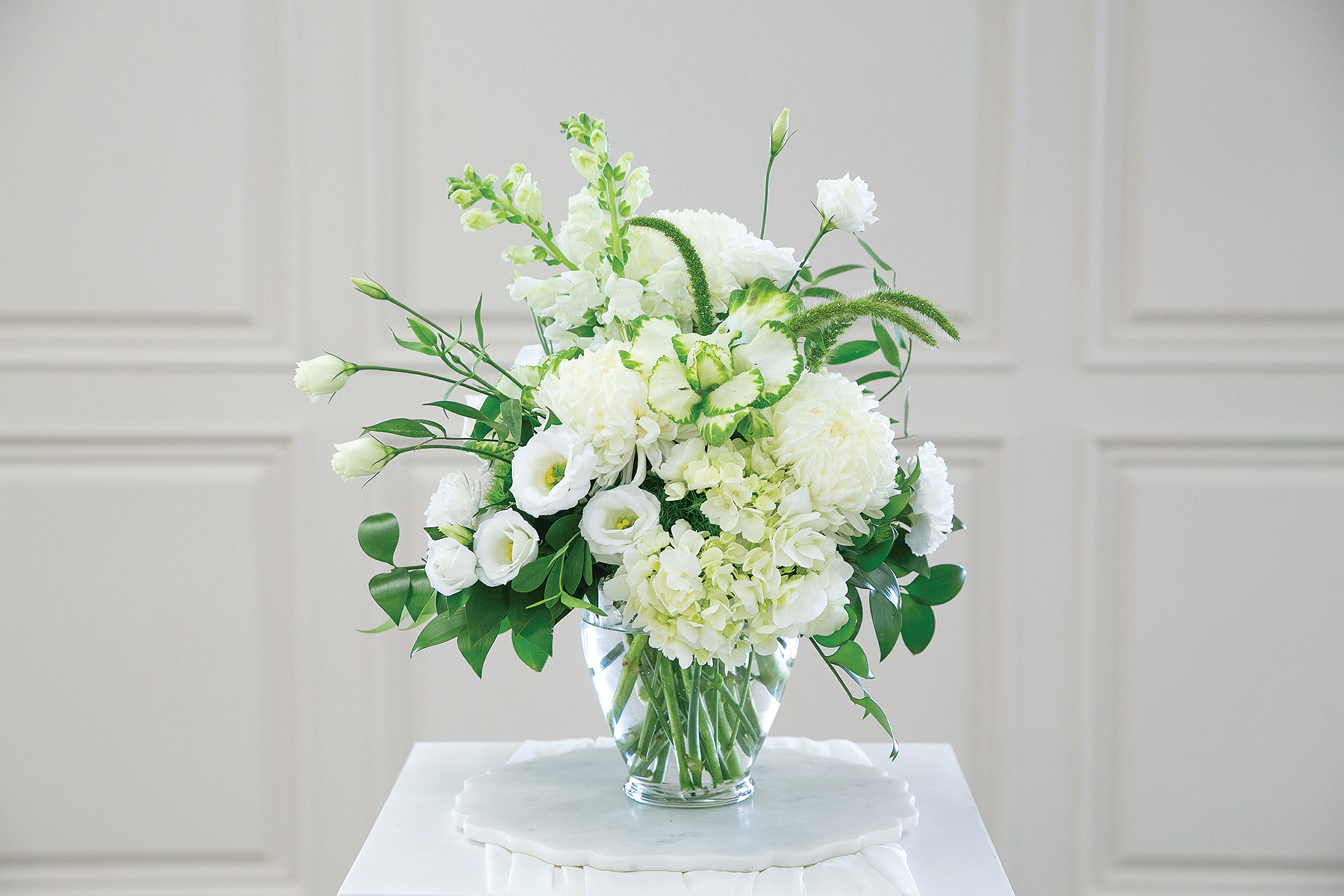 Bouquet of white and green flowers in a clear vase on a white surface with a light gray background