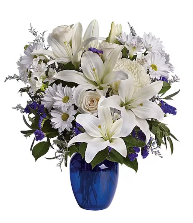 A floral arrangement featuring a cobalt blue glass vase, with a selection of white and purple flowers including lilies and eucalyptus.