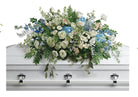 White casket with a large floral casket spray of white and blue flowers.