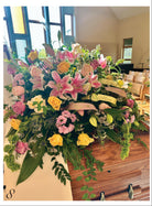 Colorful floral arrangement atop a wooden casket in a church setting with wooden pews.