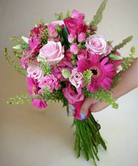 A person holding a prom posy bouquet with a variety of flowers including gerberas and roses, predominantly in pink and white colors.
