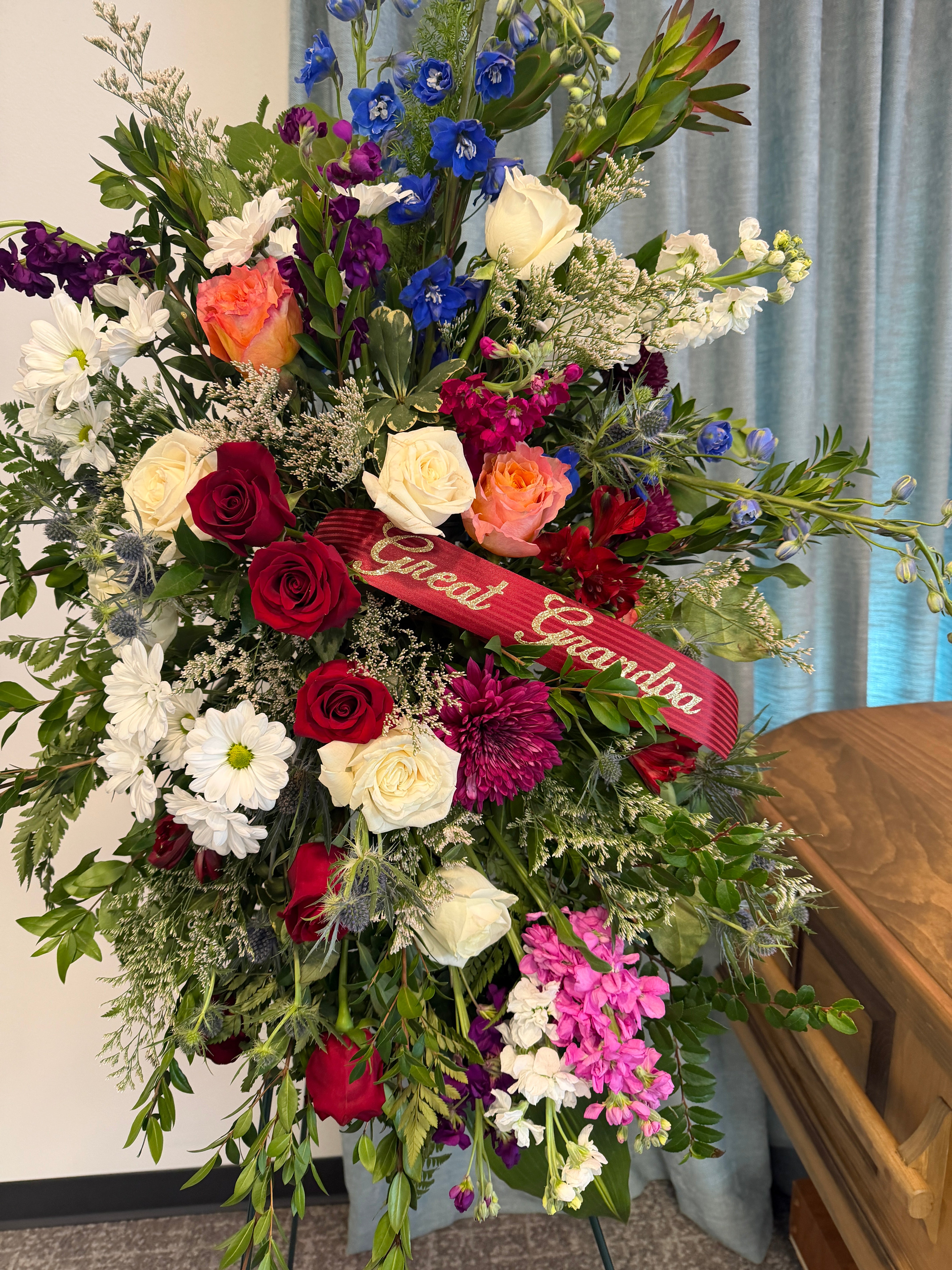 Colorful floral arrangement with a red ribbon on an easel for a funeral. 