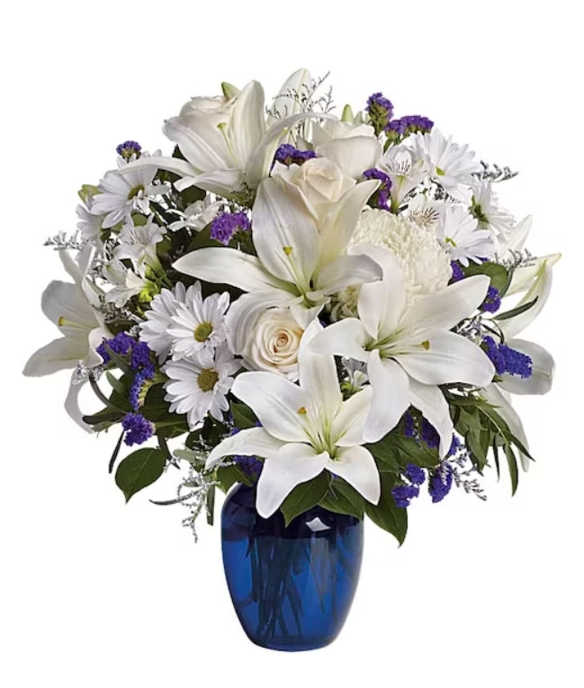A floral arrangement featuring a cobalt blue glass vase, with a selection of white and purple flowers including lilies and eucalyptus.