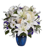 A floral arrangement featuring a cobalt blue glass vase, with a selection of white and purple flowers including lilies and eucalyptus.