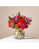 A brightly colored floral arrangement featuring a glass vase, with a variety of flowers including red and pink roses and other small blooms.