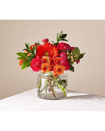 A brightly colored floral arrangement featuring a glass vase, with a variety of flowers including red and pink roses and other small blooms.